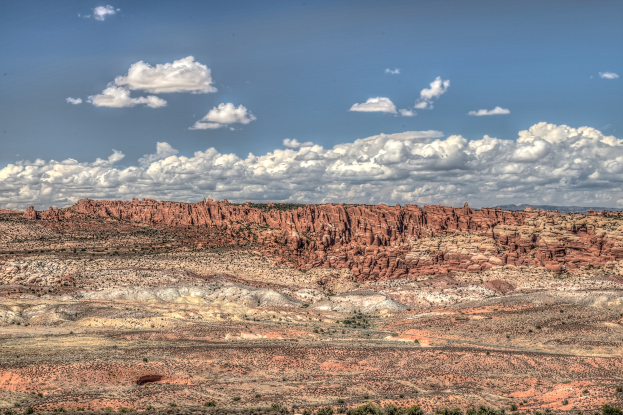 Wüstenlandschaft mit roten Felsen und spärlichen Bäumen im Vordergrund, bewölkter Himmel im Hintergrund und ein Wasserzeichen unten.