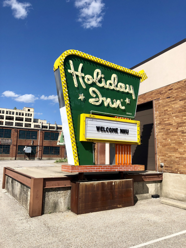 Holiday Inn Schilder an der Seite eines Gebäudes mit einem Fußwegschild davor, bewölkter Himmel und Fenstern im Gebäude.
