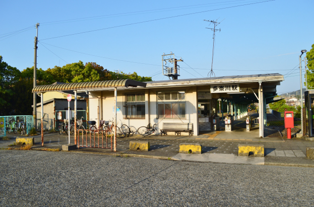 Ein Bahnhof mit Fahrrädern vorne, einer Straße unten und Häusern, Bäumen, Pfählen, Drähten und einem klaren blauen Himmel im Hintergrund.