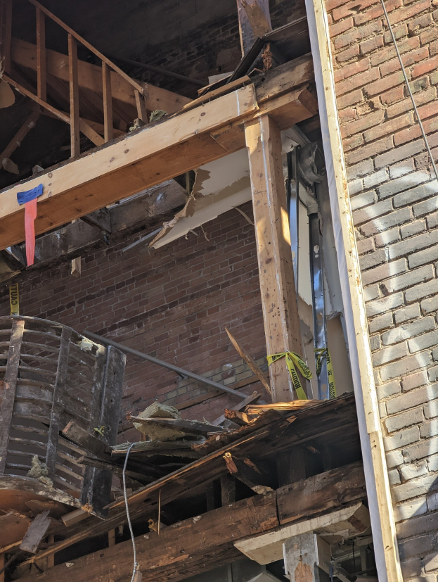 Teilweise abgerissener Bau mit verstreuten Holzplanken und Trümmern, zerbrochene Fenster und Türen.