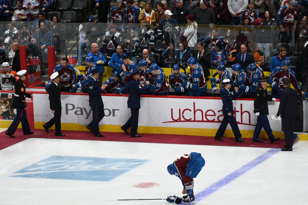 Eishockeyspieler auf dem Eis umgeben von Teamkollegen und Gegnern, mit Zuschauern im Hintergrund während eines Spiels zwischen Colorado Avalanche und San Jose Sharks am 24. März 2015.