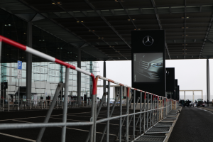 Eine Mercedes-Benz-Ausstellung auf der IAA in Frankfurt mit Fahrzeugen, Geländern, Pfosten, Schildern, Lampen und einem Gebäude im Hintergrund, bei dem der Himmel oben sichtbar ist.