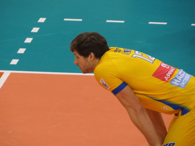 Eine professionelle Volleyballspielerin in einem gelben T-Shirt mit der Aufschrift "Volleyball" steht selbstbewusst auf einem Court und bereitet sich darauf vor, den Ball zu servieren.