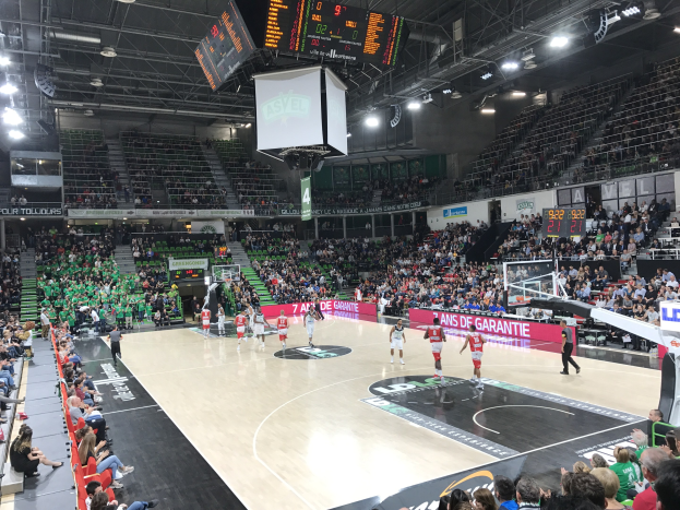Basketballspiel in einer großen Arena mit Zuschauern, mit einem Scoreboard, das "Asvel vs Galatasaray" während eines Spiels anzeigt.