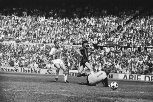 Schwarzes und weißes Bild von Männern, die auf einem Feld Fußball spielen, mit Zuschauern im Hintergrund und einem Banner mit der Aufschrift "Bundesliga 1978-79 Ajax 1-1 Hannover 96."