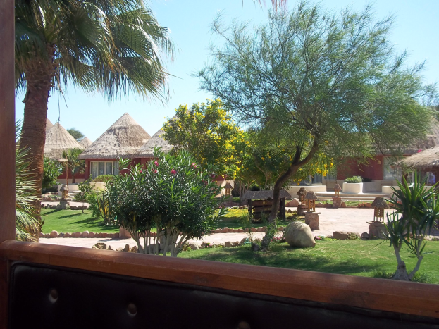 Ein Resort-Bild mit Hütten, Grün, Felsen, einer Bank und Himmel im Hintergrund.