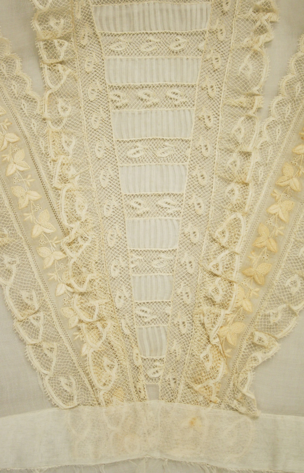 Nahaufnahme eines weißen Kleides mit zarter, kunstvoller Spitzenverzierung, die verschiedene Formen und Muster auf einem leichten, luftigen Stoff aufweist.