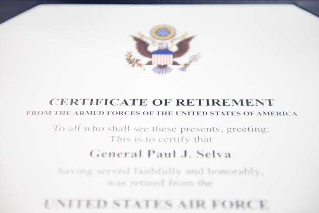 Rahmenurkunde über den Ruhestand der United States Air Force mit blauem Rand, die ein zentrales Sternschild-Logo zeigt, umgeben von einem Lorbeerkranz und einer 'Ruhestand'-Bannertafel, alles in schwarzer Tinte auf weißem Papier.