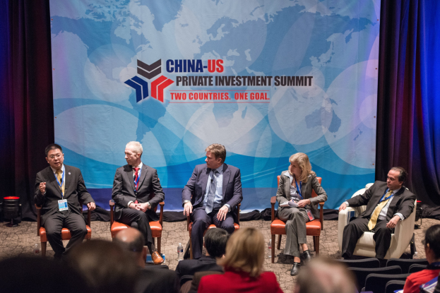 Eine Gruppe von Menschen, die auf Stühlen sitzen und auf einen Bildschirm schauen, auf dem Text und eine Karte angezeigt werden, mit Vorhängen im Hintergrund, während es scheint, dass es sich um einen China-US-Privatinvestment-Gipfel handelt.
