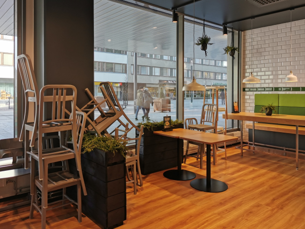 Ein Restaurantinnenraum mit hölzernen Tischen und Stühlen in der Nähe eines großen Fensters, das auf eine Berliner Straße mit Fußgängern, Gebäuden und urbanen Elementen blickt.