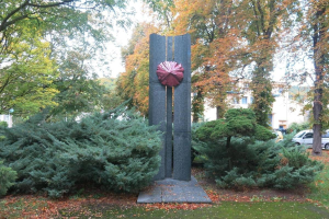 Große Metallskulptur inmitten eines Parks mit Bäumen, Pflanzen und zerrissenen Blättern, umgeben von Gebäuden und einem klaren blauen Himmel, Teil der Kunst der Stadt Berlin.