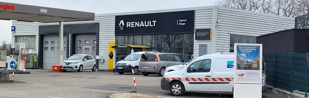 Ein Renault-Autohaus mit parkenden Autos davor, umgeben von einem Metallzaun, mit einem Schild, Pfosten, einer Texttafel, Bäumen und einem bewölkten Himmel.