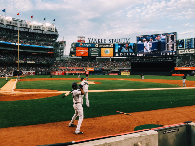 Baseballspiel im Gange im Yankee Stadium mit Spielern auf dem Feld und Zuschauern in den Rängen unter einem bewölkten Himmel.