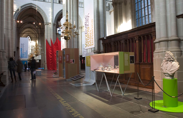 Ein geräumiger Museumsraum mit verschiedenen Ausstellungsstücken, darunter eine Statue auf einem Sockel, steht mit Seilen, Bannern, Säulen und Kronleuchtern, mit wenigen Besuchern.