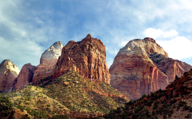 Eine malerische Aussicht auf den Zion-Nationalpark in Utah mit majestätischen Bergen, üppigen Bäumen, steinigem Gelände und einem Himmel mit weißen Wolken.