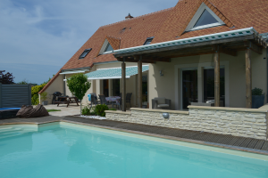 Ein Gebäude mit einem Esstisch und Pflanzen davor, einem Pool und einem bewölkten Himmel darüber.