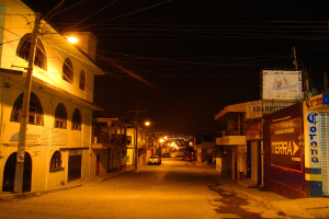 Eine Straßenszene mit Gebäuden und Strommasten auf beiden Seiten, einige parkende Fahrzeuge vor den Gebäuden und eine Straße in der Mitte.