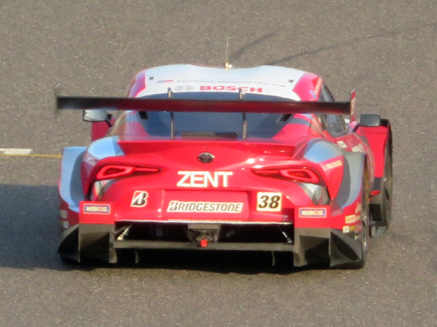 Ein roter Sportwagen mit Text und Zahlen nimmt an den 24 Stunden von Le Mans teil und fährt auf einer Rennstrecke.