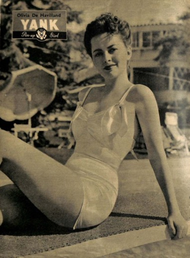 Olivia de Havilland in einem Badeanzug sitzend auf dem Boden mit einem Lächeln, umgeben von Bäumen, Stühlen, einem Gebäude und Text oben.