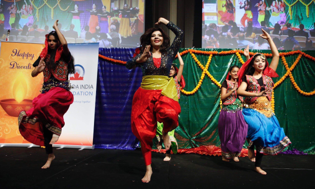 Junge Mädchen tanzen traditionell auf einer Bühne während einer Diwali-Feier, umgeben von Bannern, Girlanden und einem Publikum im Hintergrund.