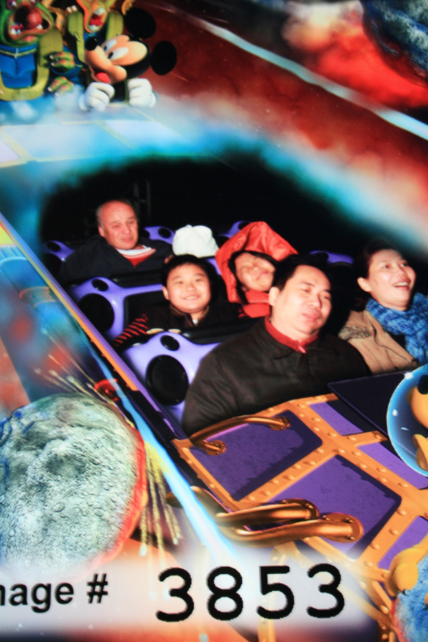 Gruppe von Menschen auf einer Achterbahn mit Mickey Mouse-Figuren im Hintergrund und Text unten.