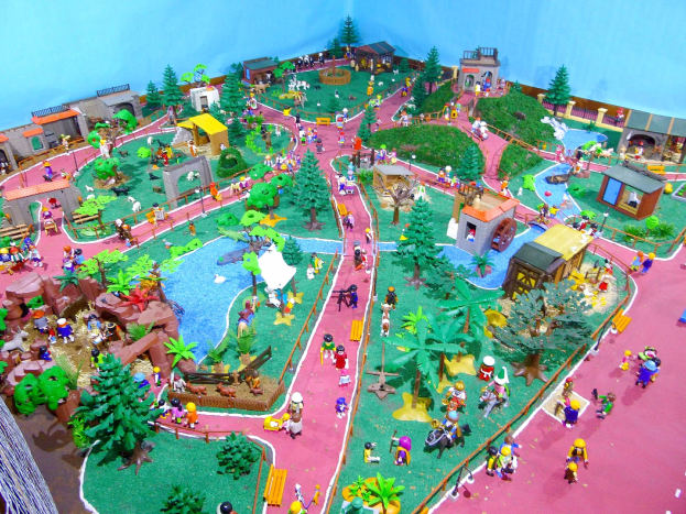 Ein Miniaturmodell eines Zoos mit Menschen, Bäumen, Häusern, Pflanzen, Gras, einem Zaun und einer Wand, mit Text unten.