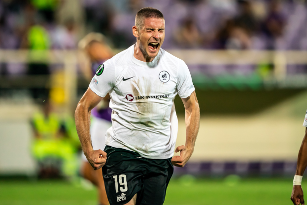 Ein Mann in weißem Hemd und schwarzen Shorts rennt auf einem Fußballfeld, umgeben von einer Gruppe von Menschen, die ein Tor feiern, während eines Spiels zwischen Leeds United und Melbourne Victory.