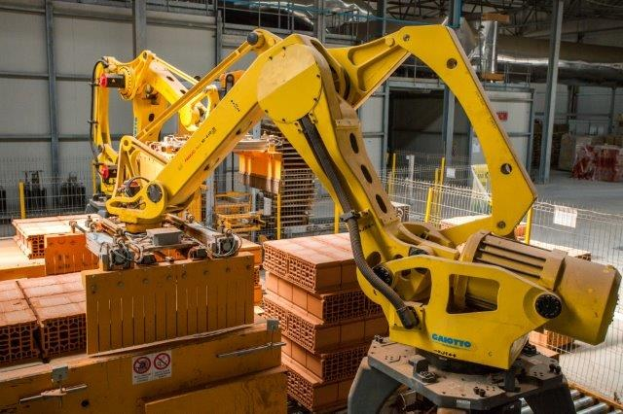 Industrielles Lager mit gestapelten Kisten, Kränen, Zaun, Pfählen und einer fernen Wand in einer Fertigungsanlage.