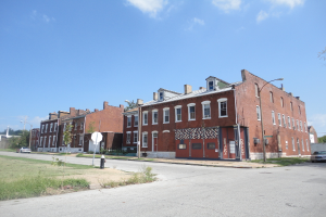 Ein Geb√§ude mit Stra√Ÿenlaternen, Masten und B√§umen, mit Fahrzeugen auf beiden Seiten, einem Weg und Gras unten und einem Himmel oben.