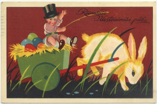 Alte Postkarte mit einem Baby in einem Zylinder, das einen mit bunten Ostereiern gefüllten Handkarren schiebt, begleitet von einem Kaninchen, mit handgeschriebenen Ostergrüßen.