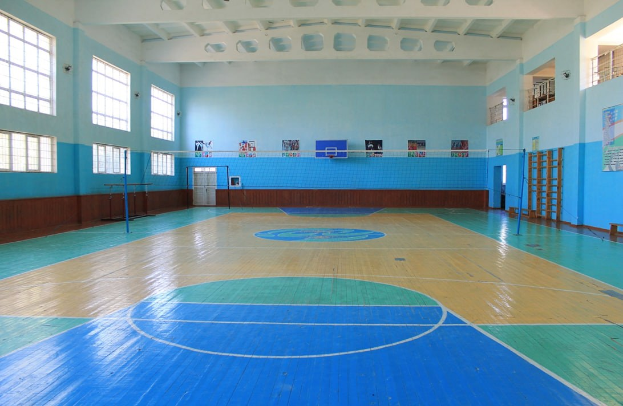 Großer Turnhallen mit blau-weißem Boden, Basketballfeld, Netz mit Pfosten, Tür, Fenstern, Wandplakaten, Geländer und Dach.