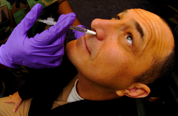 Ein Arzt in lila Handschuhen verabreicht einem Mann eine Impfung durch Injektion in den Mund.