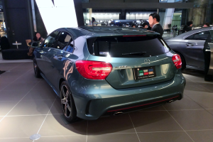 Ein Mercedes-Benz A-Klasse Schrägheck in Frankfurt, glänzend schwarz mit Chromakzenten, niedriger Profil, breite Basis, markantes Grill und Aluminiumräder, umgeben von einer Gruppe von Menschen.