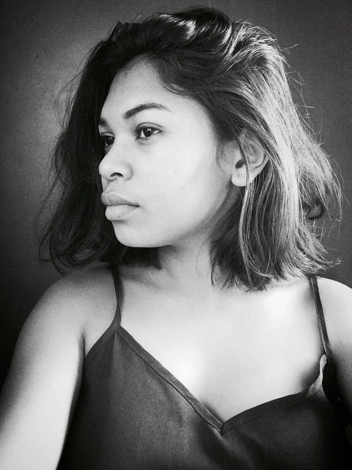 Eine selbstbewusste Frau in einem schwarzen Kleid posiert in einem Schwarz-Weiß-Foto vor einer Wand und strahlt Selbstvertrauen aus. Ihr glatter Bob und das natürliche Make-up unterstreichen das Bild.