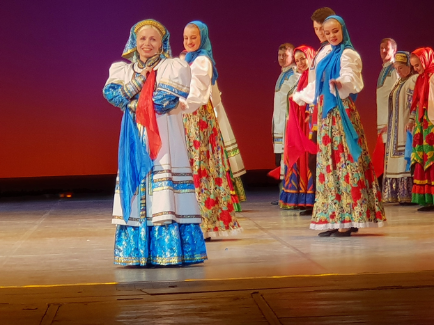 Eine Gruppe von Menschen in buntem, detailliertem traditionellem ukrainischem Kostüm, die auf einer Bühne lächeln und stehen.