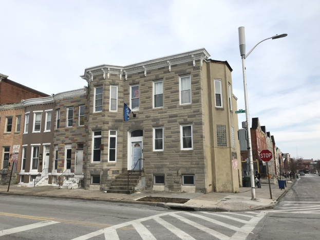 Reihe moderner Häuser an einer Straßenecke in Philadelphia, mit Fahrzeugen, Bäumen und einem bewölkten Himmel im Hintergrund.