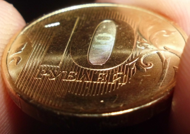 Eine Person hält eine Goldmünze in der Hand vor einem dunklen Hintergrund.