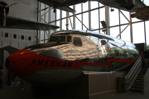 Ein American-Airlines-Flugzeug in einem Museum mit Menschen drumherum, Treppe auf der rechten Seite und einem Gebäude, Bäumen und einem klaren blauen Himmel im Hintergrund.