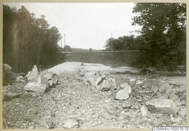 Schwarzes und weißes Foto einer Schotterstraße in Germantown, New Jersey, mit Steinen, Bäumen, Strommasten, einer Wand und Himmel im Hintergrund und einer Liste von nummerierten Routen unten.