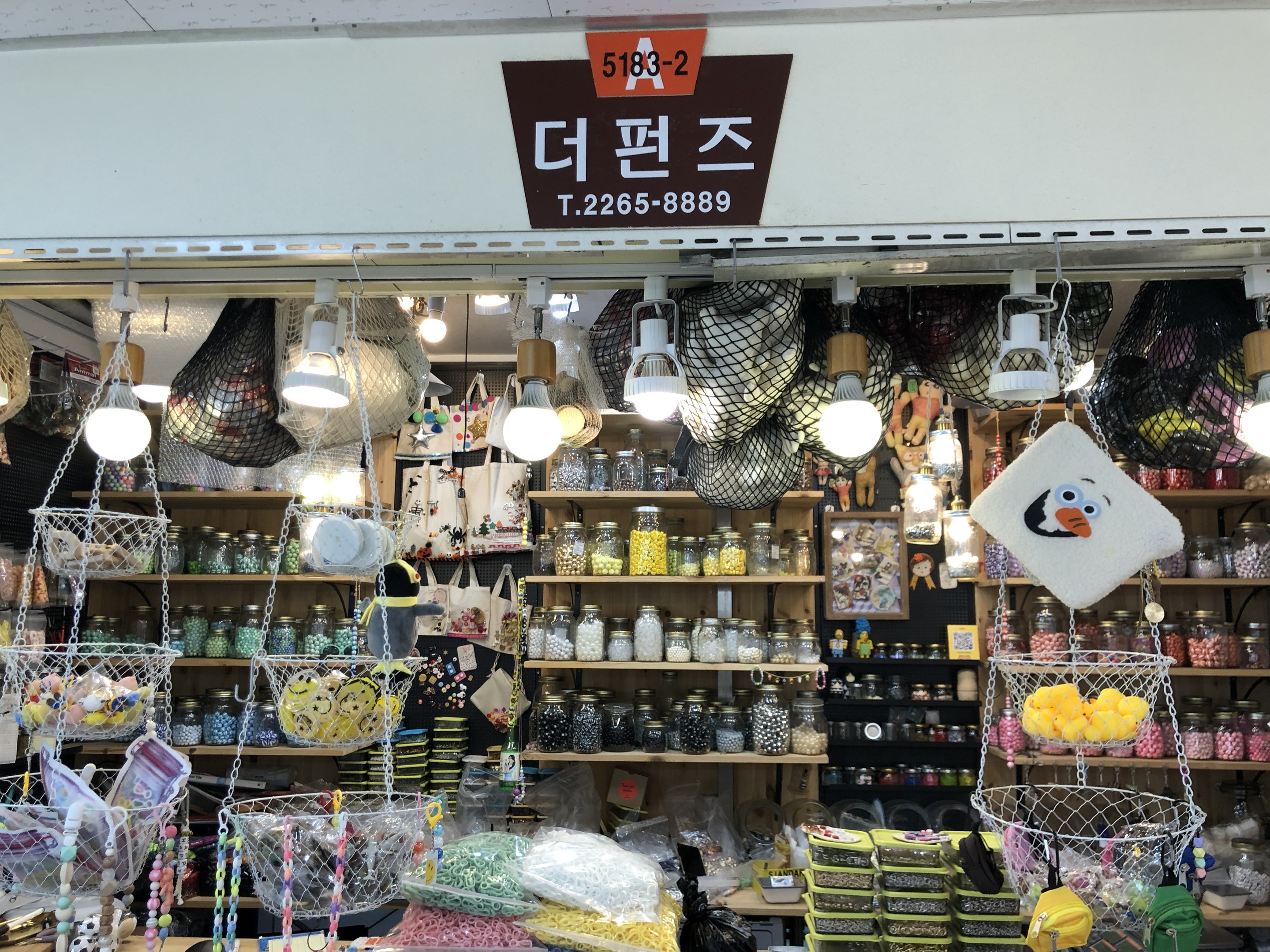 Ein unordentlicher Laden in Seoul zeigt verschiedene Gegenstände wie Körbe, Lampen, Flaschen und Spielzeuge auf Regalen, mit einer Tafel oben, die ihn als einen der besten koreanischen Läden ausweist.
