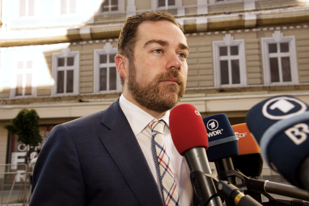 Ein Mann im Anzug spricht vor einem Gebäude zu den Medien und scheint auf eine dreijährige Haftstrafe zu reagieren.