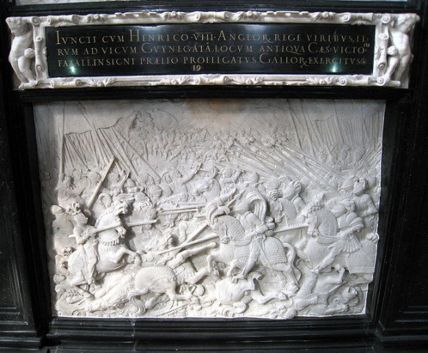 Weißer Marmorplakette an der Seite eines Gebäudes, die eine Kampfszene mit Figuren zeigt, die Schwerter und Schilde schwingen, umrahmt von einem schwarzen Rand, umgeben von Zuschauern.