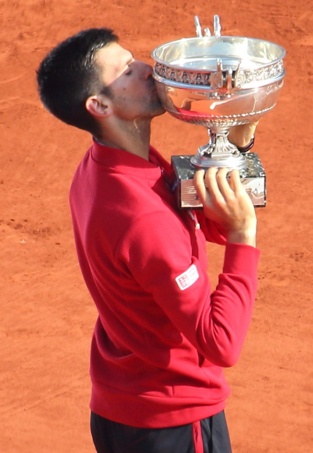 Novak Djokovic hält den French-Open-Pokal nach seinem Sieg gegen Rafael Nadal im Finale der Herren-Einzel, küsst den Pokal mit einem triumphierenden Gesichtsausdruck.