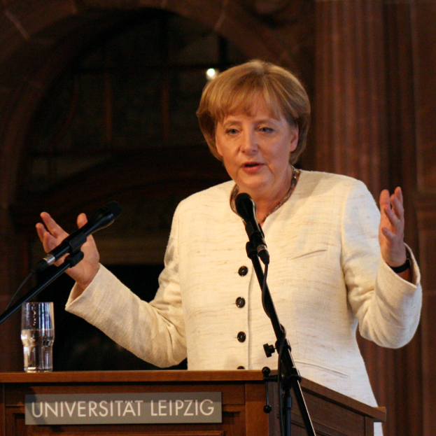 Bundeskanzlerin Angela Merkel hält eine Rede an der Universität Leipzig, vor einem Rednerpult mit einem Mikrofon und einem Glas Wasser.