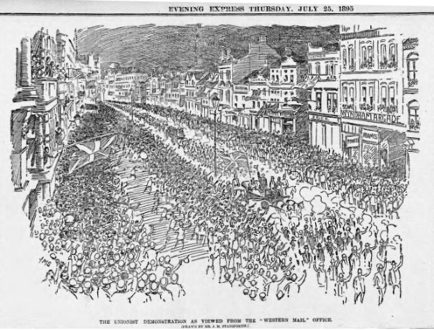 Schwarzes und weißes Bild einer Menge, die zwischen Gebäuden die Straße entlang geht, mit Text oben und unten: "Die Unionistendemonstration, wie sie vom Western Mail Office aus zu sehen ist."