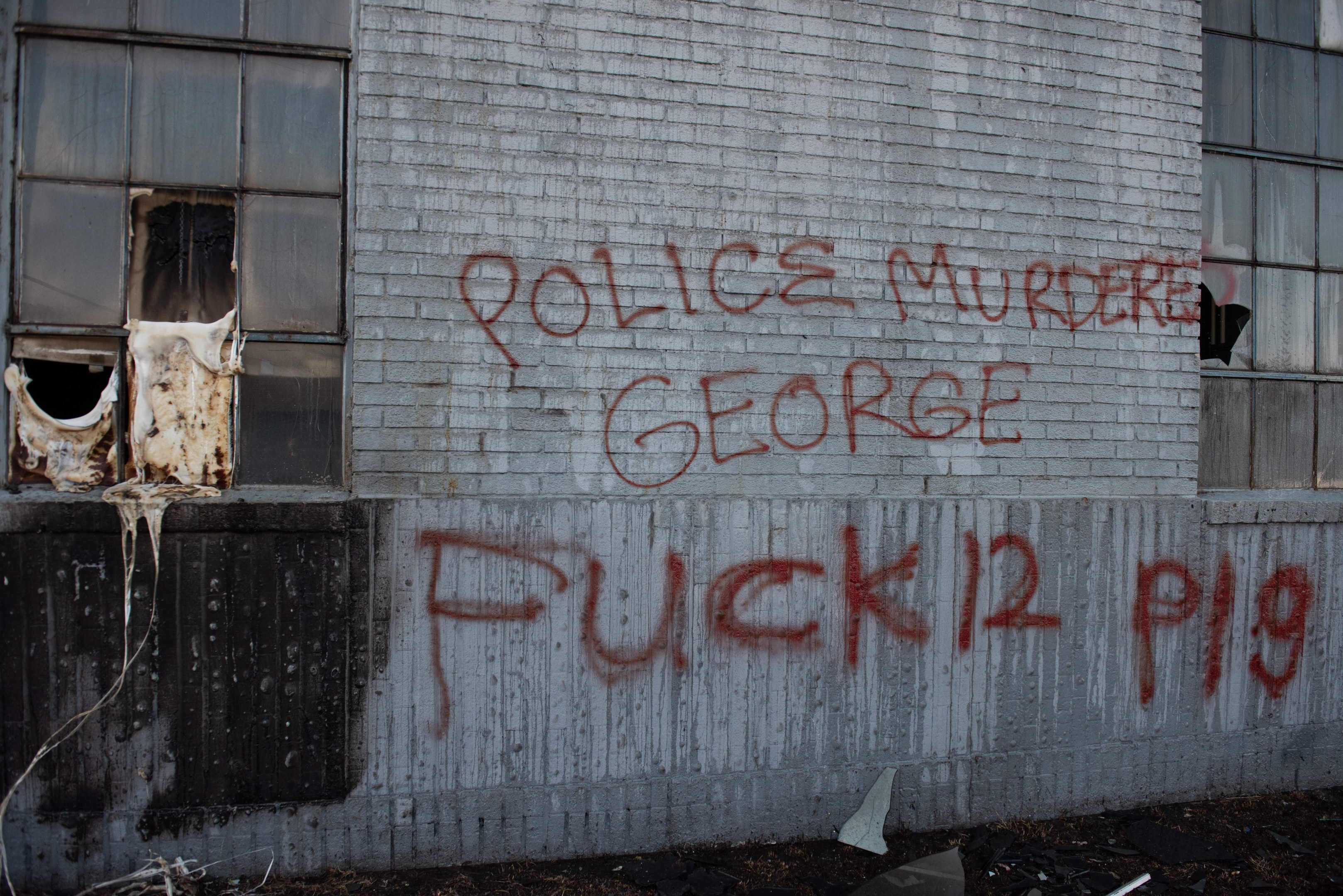 Graffiti an einer Gebäudewand mit der Aufschrift "Polizeimord George Fuck 12 P19" mit Fenstern und verstreuten Gegenständen davor.