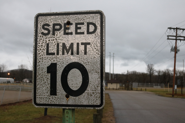 Geschwindigkeitsbegrenzungsschild am Straßenrand mit umgebenem Gras, Strommasten, Häusern, Bäumen und einer bewölkten Himmel.